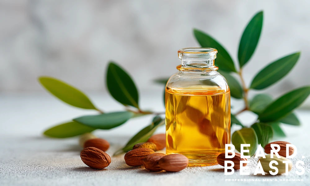 Glass bottle of golden jojoba oil with raw jojoba seeds and green leaves on a textured light background, styled for natural beard care products