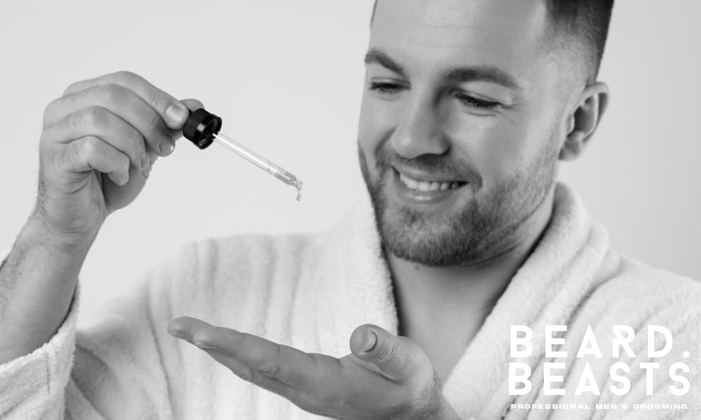 Man in a white robe applying beard oil with a dropper, illustrating hydration and conditioning benefits for beard and skin.