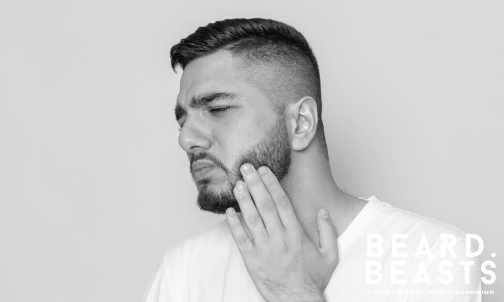 Man touching beard with discomfort, showing irritation from beard itch during early growth phase