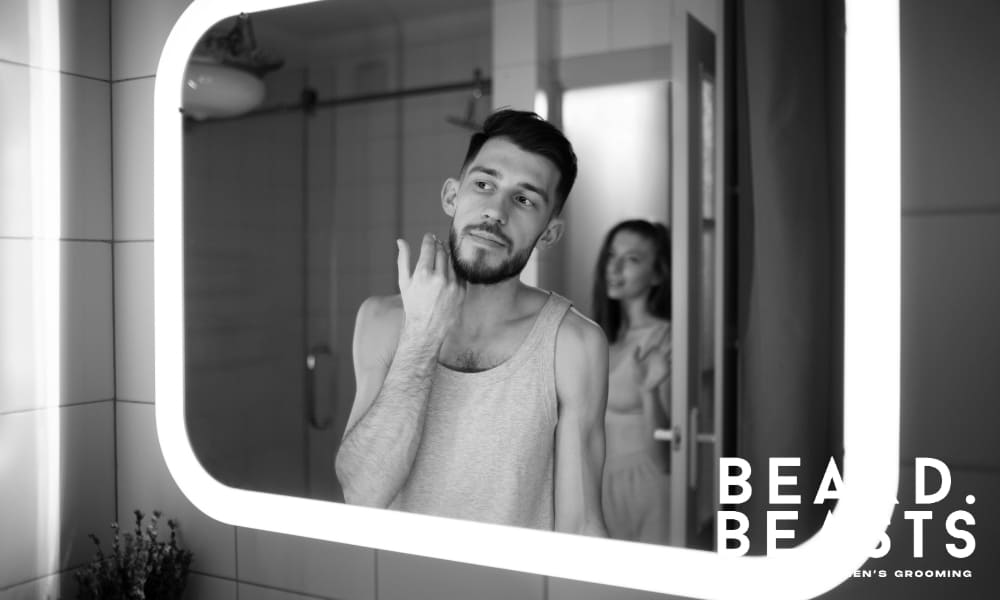 Man examining early beard growth in the mirror, illustrating the first stage of how to grow a full beard