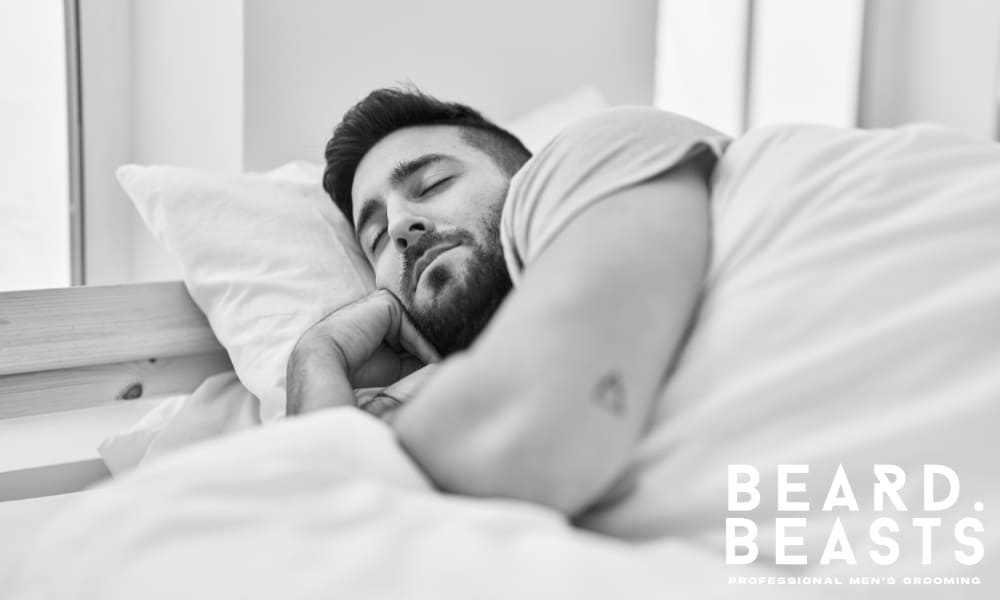 Young man with a beard sleeping peacefully in bed—rest is essential for healthy beard growth and hormone balance.