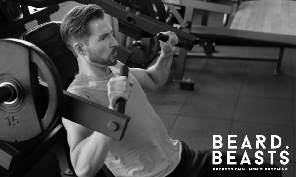 Bearded man working out in gym with focused expression, symbolizing discipline and commitment to beard growth goals