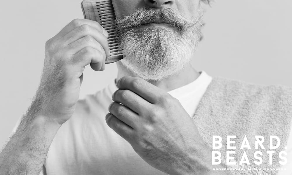 Older man grooming his full white beard, illustrating lifelong mastery of how to grow a full beard