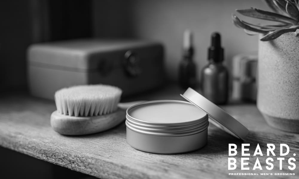 tin of balm stored on a wooden shelf next to grooming brush, dropper bottles, and potted plant