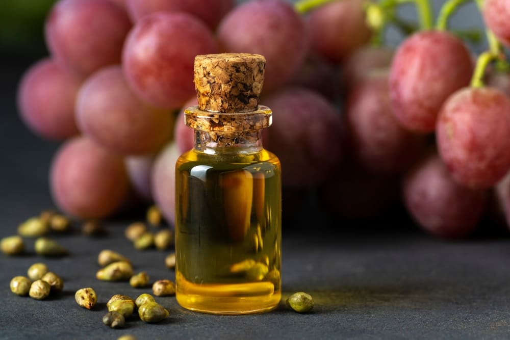 Small glass bottle filled with golden grapeseed oil, surrounded by grape seeds and fresh grapes in the background, showcasing the natural ingredients used in grapeseed oil for beard care.