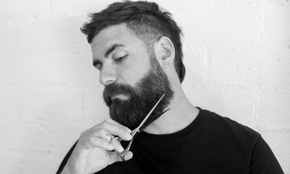 A man trimming his beard with scissors, demonstrating how to trim a beard with scissors for precise shaping and grooming.