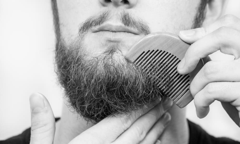 Close-up of a man using a wooden comb to groom his thick beard.