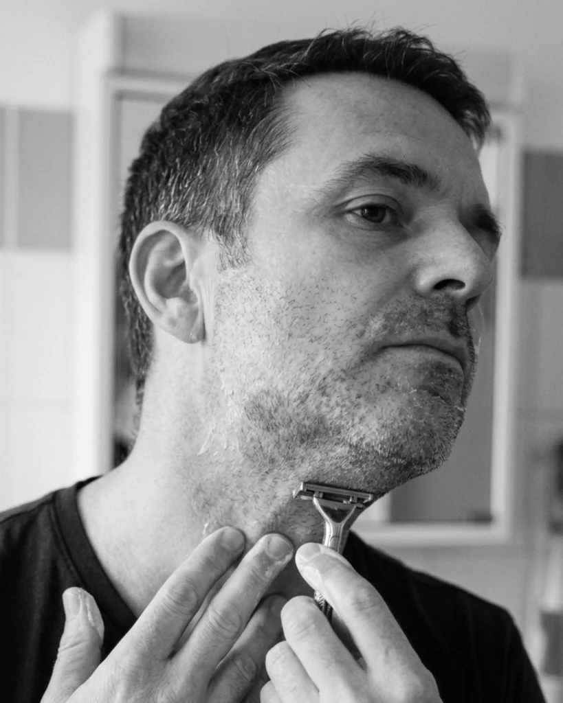 Man repeatedly shaving a stubborn neck patch with visible razor burn and redness from chasing a perfectly smooth neck