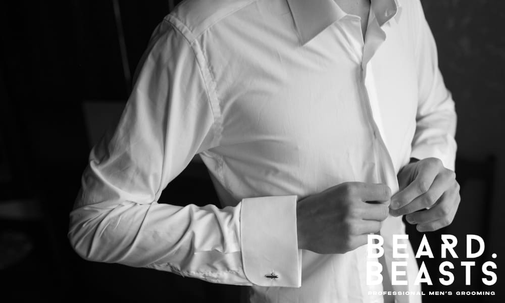 Man buttoning a white dress shirt, with the hem extending below the waistline—illustrating proper shirt length for a secure, stay-tucked fit.