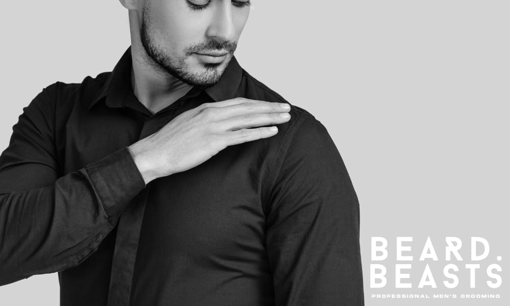 Man inspecting shoulder seam alignment on a fitted dress shirt—highlighting the importance of proper shoulder fit for clean structure and balance.