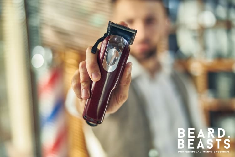 Close-up of a barber holding a red hair clipper towards the camera in a professional barbershop setting. The blurred background highlights traditional barber poles and grooming tools. The image emphasizes precision and professional grooming, ideal for tutorials on how to clean hair clippers to maintain hygiene and performance.