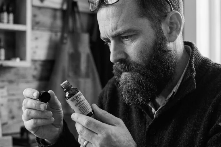 Bearded man examining a beard oil bottle for an article about beard oil ingredients
