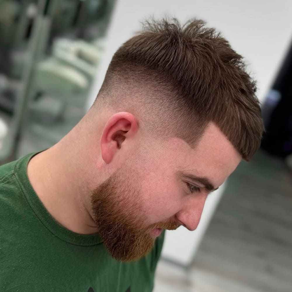 Close-up of a man with short, neatly cropped sides and a textured top, paired with a groomed beard. The look highlights clean lines and a well-balanced style for a sharp, modern appearance.