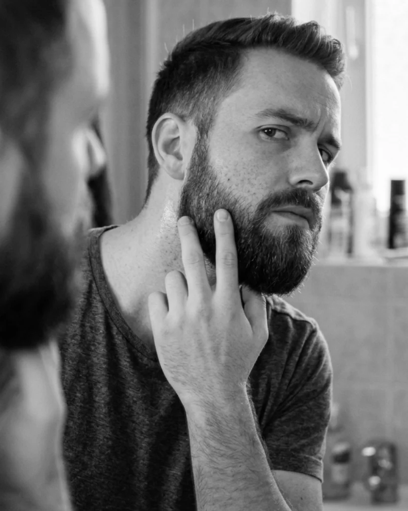 Bearded man checking mild skin irritation on his cheek after using beard oil with natural ingredients