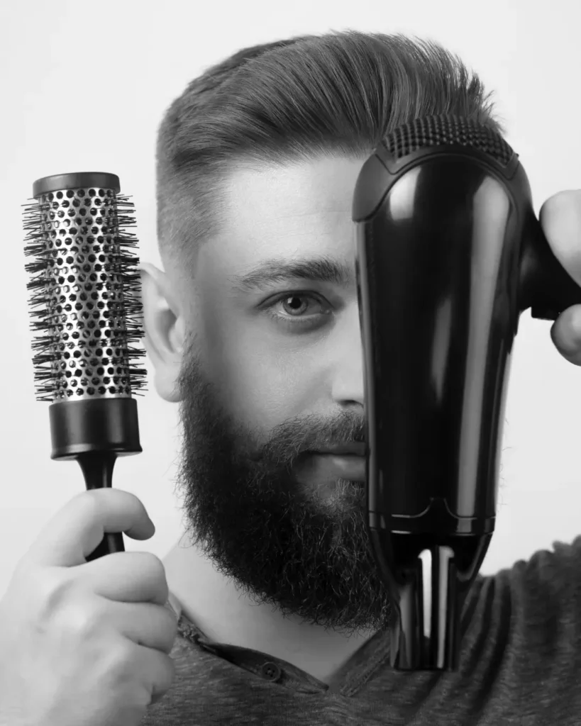 Man using a hair dryer and round brush, showing how styling effort affects the difference between a pompadour and a quiff.