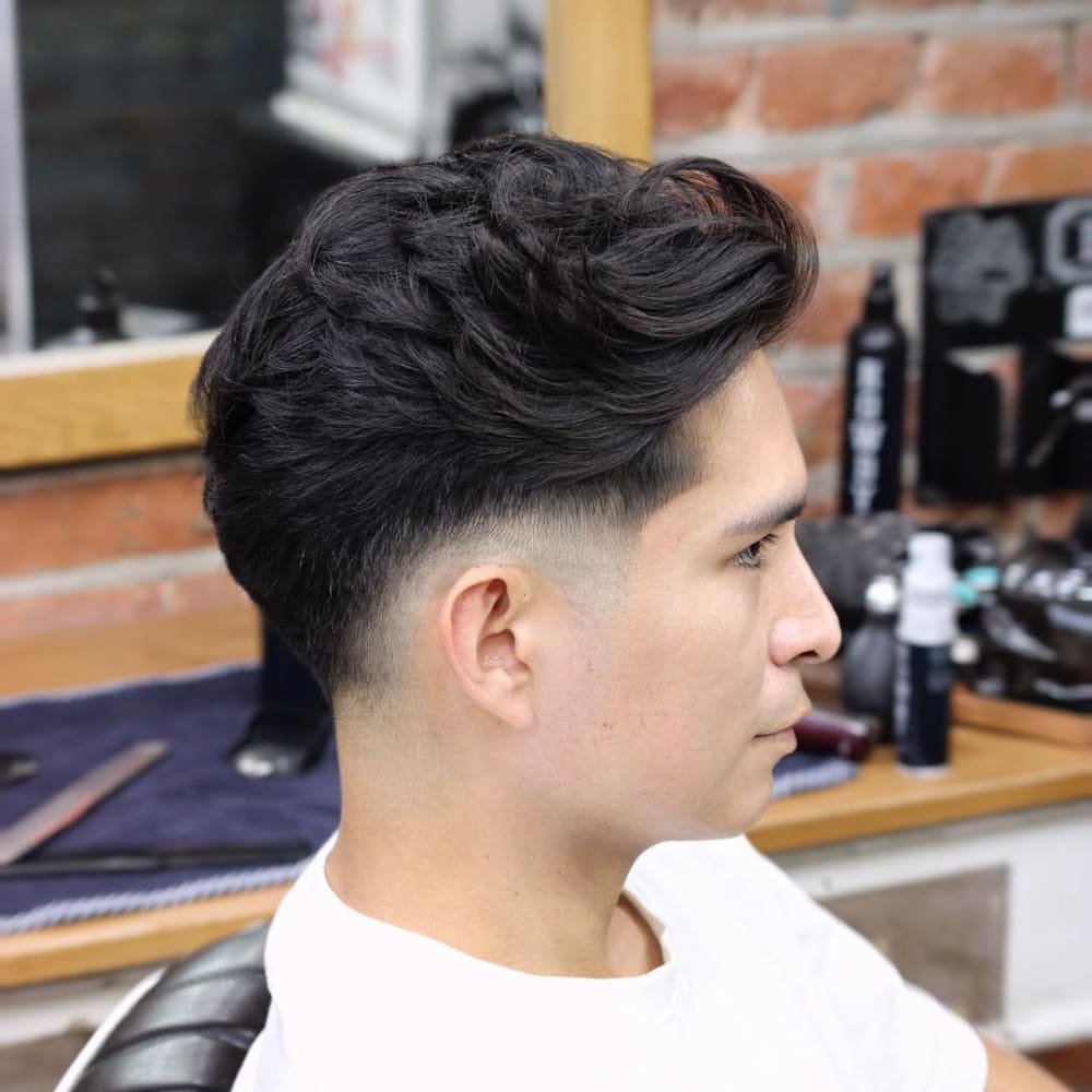 Side profile of a young man with a low fade haircut, featuring a subtle gradient that starts close to the ears and gradually blends into longer, voluminous hair on top. A fade haircut is a stylish option where the hair tapers smoothly, providing a clean and sophisticated appearance suitable for various hair textures and styles.