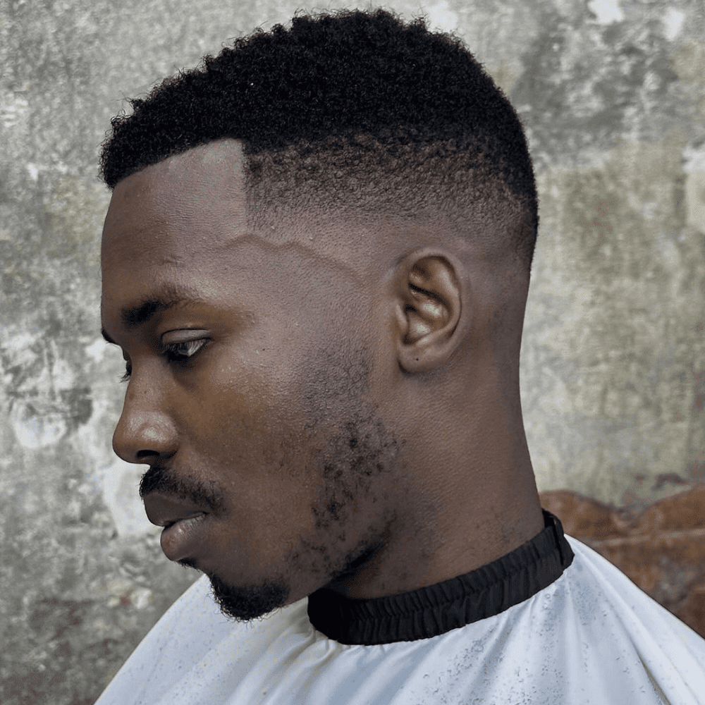 Clean, sharp line-up with a textured, natural afro on top, blended seamlessly into a taper for a fresh and stylish look.