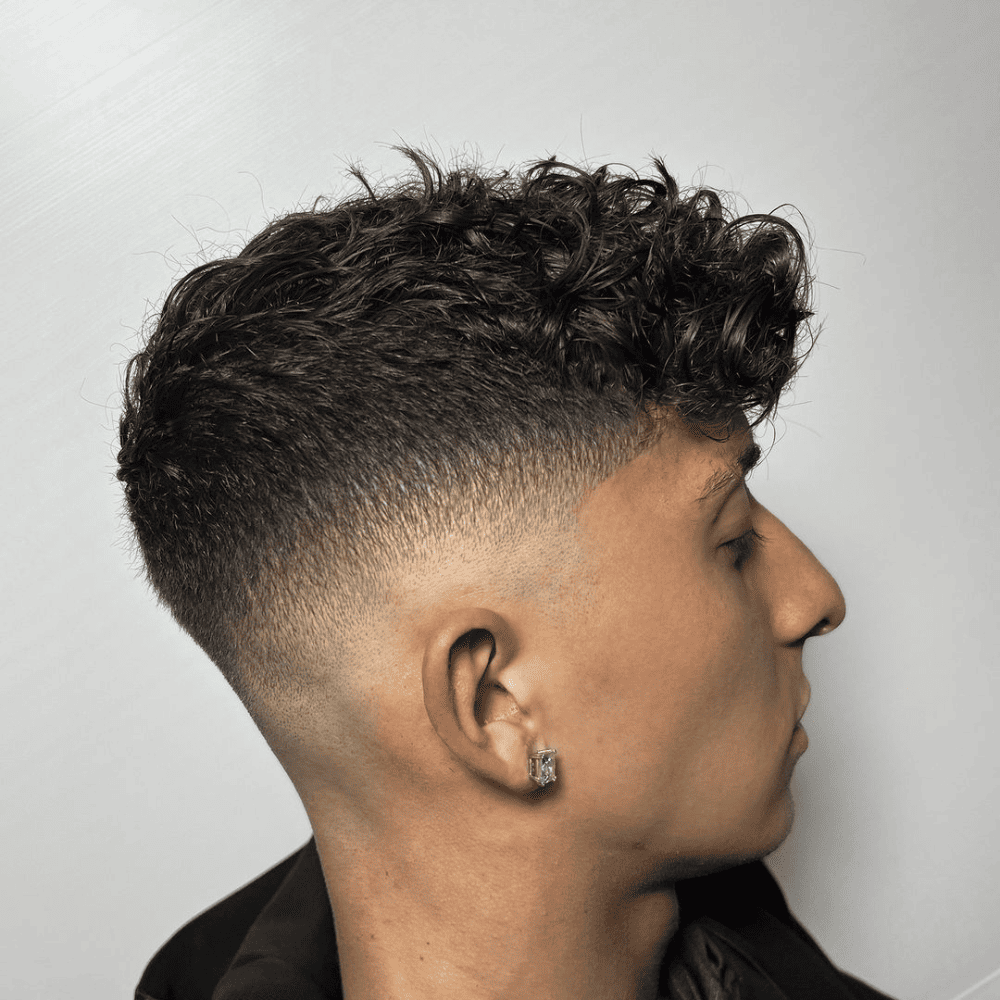 Man with curly hair on top. The hairstyle showcases a clean, gradual fade on the sides and back, blending into the natural curls on top. This stylish and modern look is ideal for men's hairstyles in 2024, highlighting the texture and volume of curly hair.