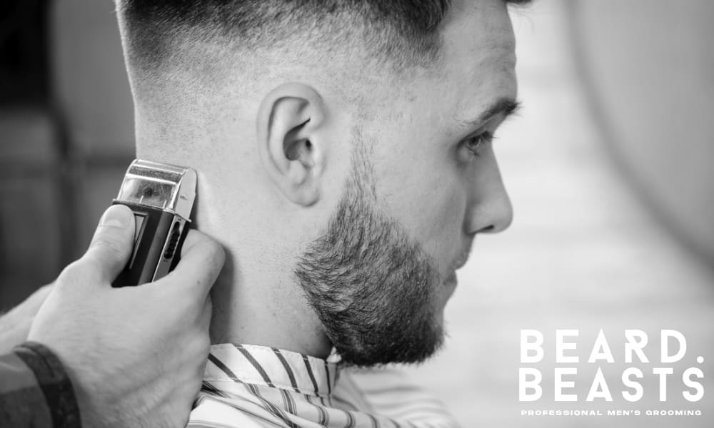 Barber finishing a man's haircut with clippers, focusing on the neck and sideburn area.