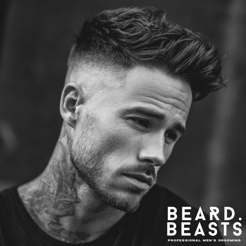 Man with a sharp high fade haircut that tapers to skin, styled with a voluminous quiff on top.