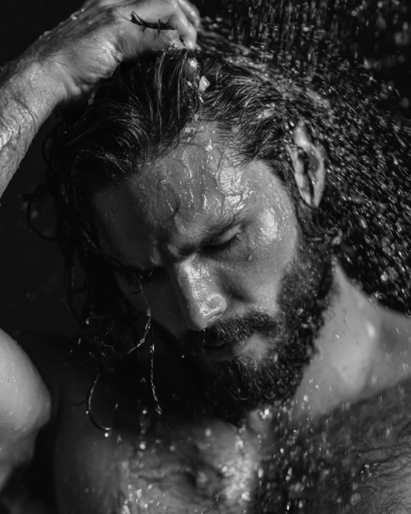 Bearded man washing his hair in the shower as part of a men’s hair care routine
