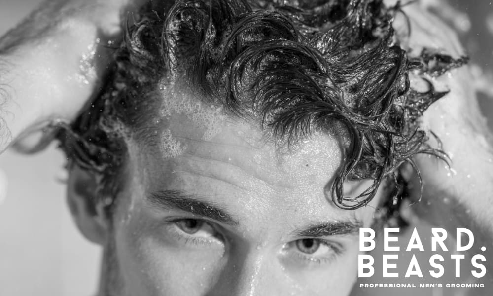 Man washing his hair in the shower, ensuring clean, textured hair for a fresh look.