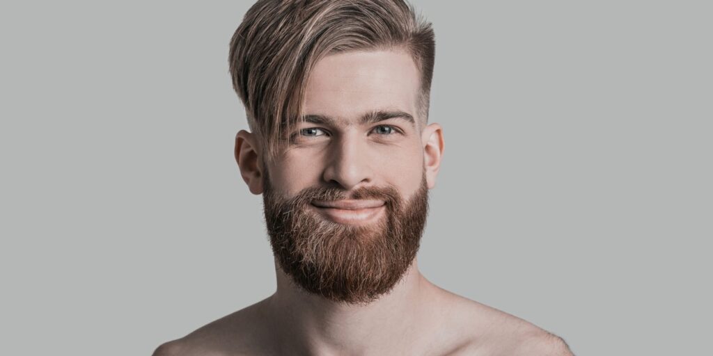 Close-up portrait of a man with a stylish, asymmetrical haircut featuring a long fringe swept to the side and a neatly groomed beard. This image highlights modern men's hair care and grooming trends, showcasing a well-maintained hairstyle and beard that reflect attention to detail and personal style. Ideal for illustrating effective hair care and grooming practices for men.