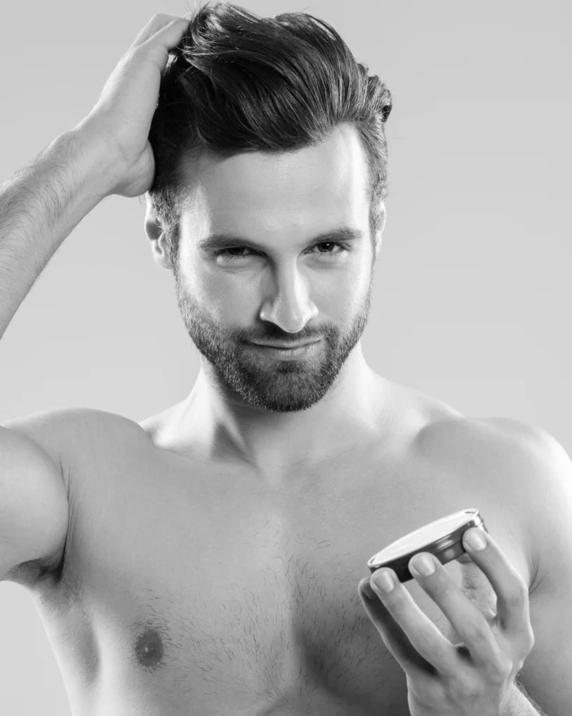 Man applying styling product to his hair while holding an open container