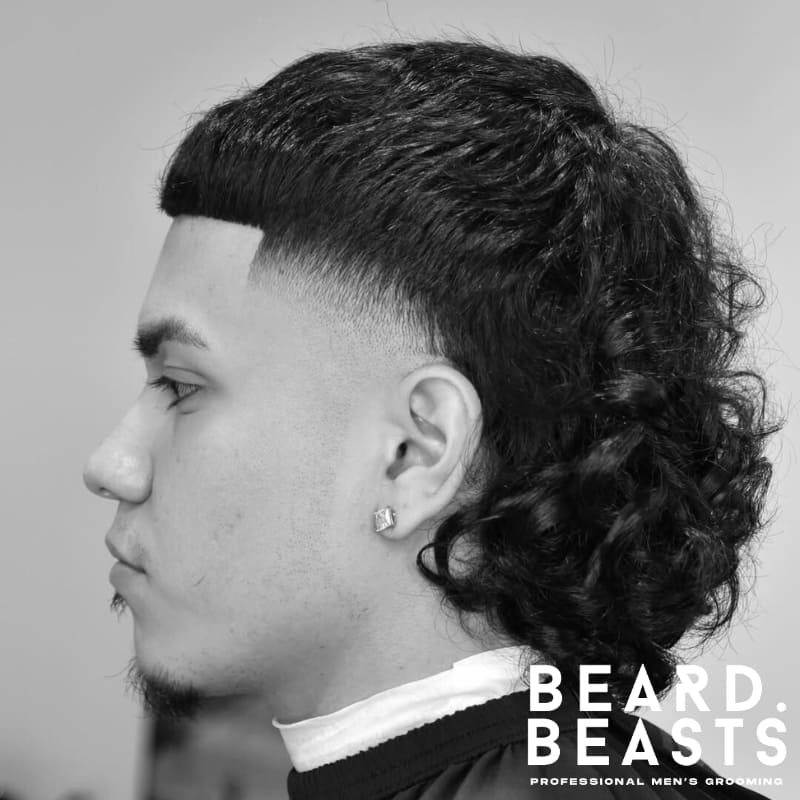Men's mullet fade haircut featuring curly hair on the back and sides with a clean fade. Perfect for those seeking a bold, unique style with a modern twist.