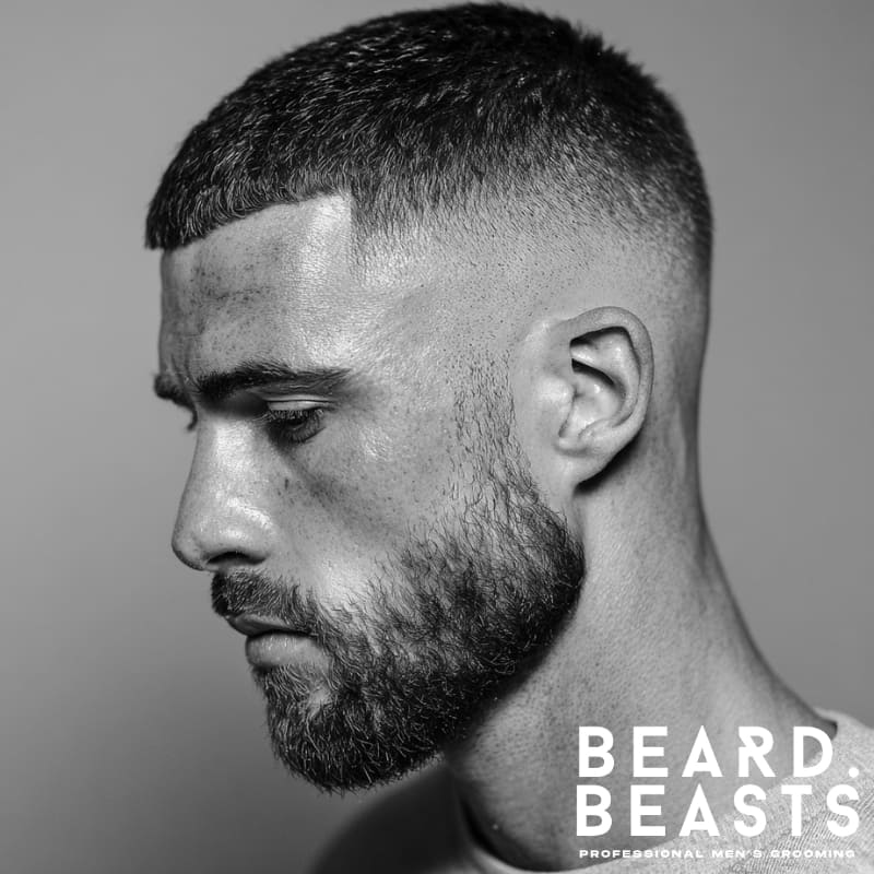 Man with a short fringe fade haircut and full beard, side profile showcasing clean, textured styling.
