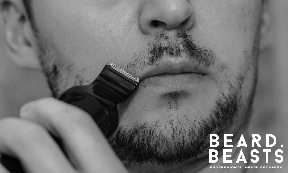 Close-up of a man trimming his mustache with an electric trimmer—illustrating a common grooming mistake when shaping different types of mustaches.