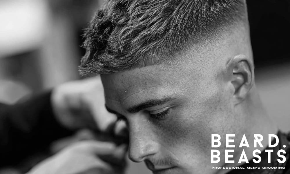 A close-up of a man, showing clean, defined lines on the sides and textured hair on top, emphasizing the contrast and precision of the haircut.
