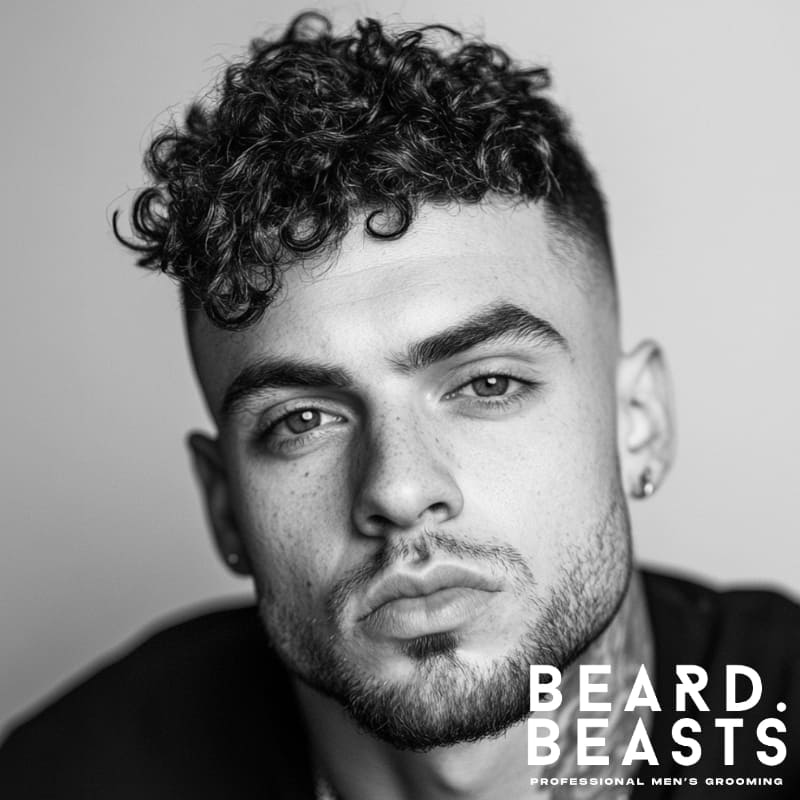 A close-up of a man with a curly high fade, featuring natural curls on top and a clean, sharp fade on the sides for a bold and modern look.