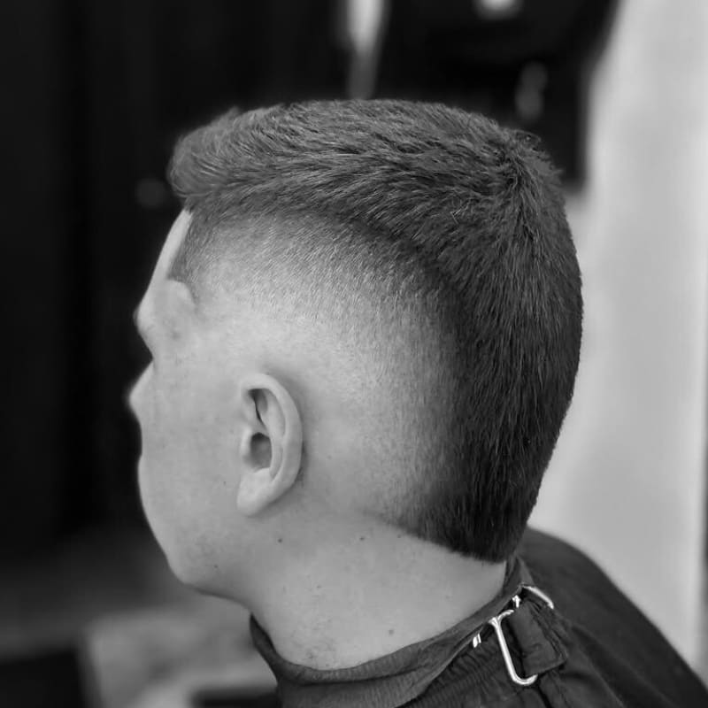 A close-up of a man with a burst fade, featuring a sharp line between the short sides and longer hair on top, with a smooth, rounded fade around the ears for a bold and dynamic look.