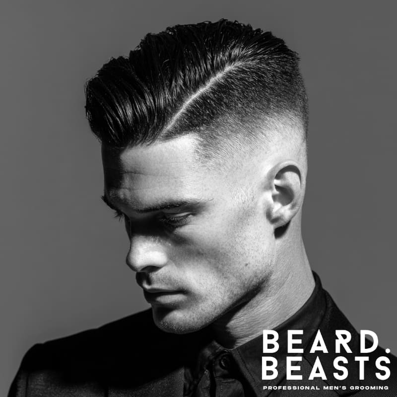 A close-up of a man with a high fade and comb-over, featuring a sharp part on the side and slicked-back hair on top for a clean, polished look.