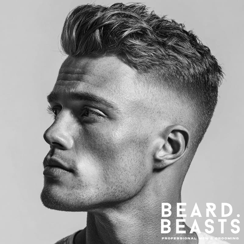 A profile shot of a man with a high fade and voluminous quiff, showcasing a sharp contrast between the clean sides and the textured, styled top.