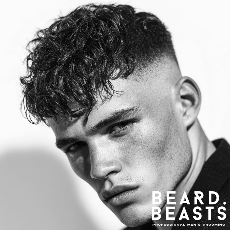 A close-up of a man with a high fade and textured fringe, showcasing a modern, sharp look with voluminous hair on top and a clean fade on the sides.