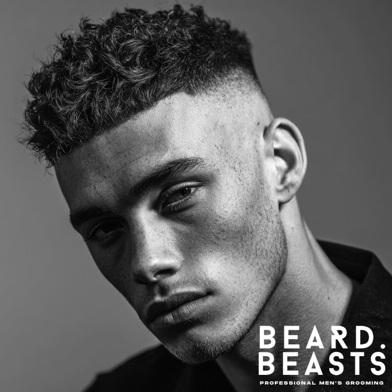 A close-up of a man with a high skin fade hairstyle, showcasing clean lines and textured curls on top. Ideal for modern, sharp haircuts in 2025.