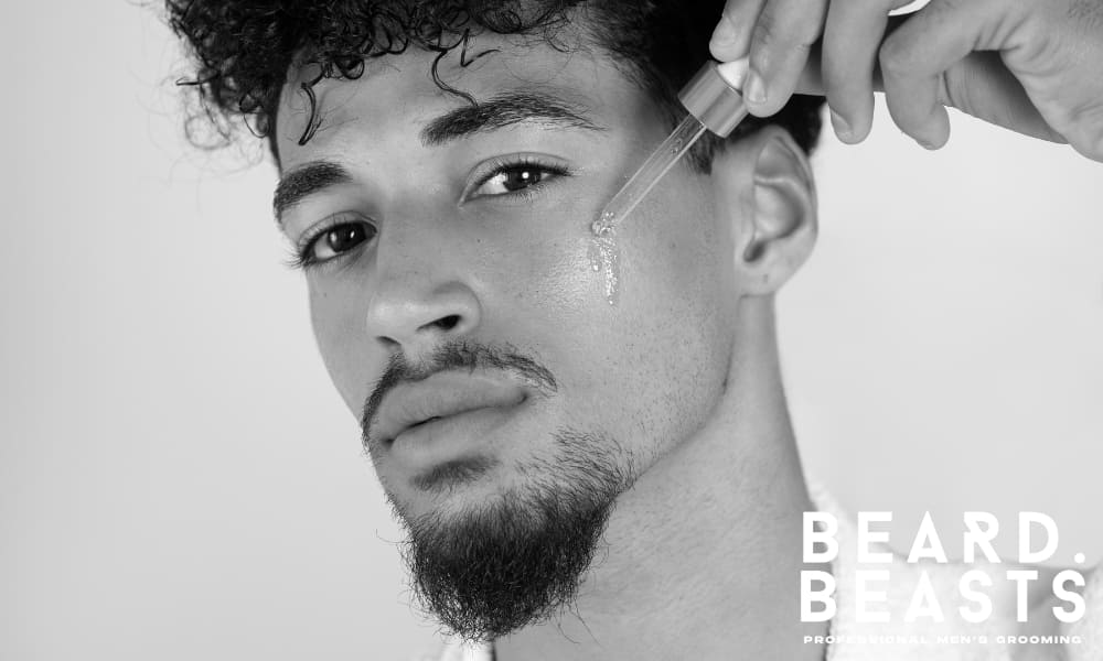Close-up of a man applying beard oil to his face—illustrating essential grooming and skincare as part of mustache maintenance for healthy facial hair.