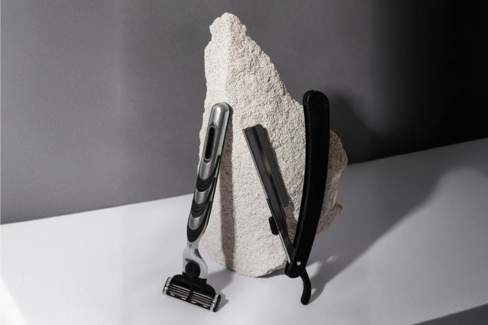 A side-by-side comparison image of a modern multi blade razor and a classic single blade razor placed against a textured stone backdrop, illustrating the differences in design and functionality in the single blade razor vs multi blade razor discussion.