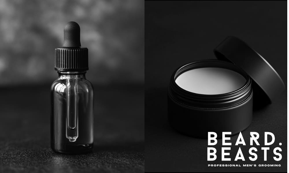 A black dropper bottle of beard oil alongside a sleek tin of beard balm, set against a dark, textured background. The image highlights the key differences when comparing beard oil vs beard balm, showcasing the contrasting textures and uses for effective beard grooming.