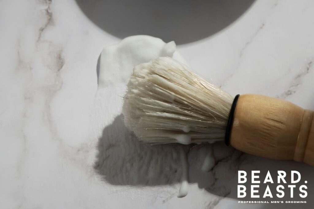 A shaving brush covered in rich shaving foam sits on a marble surface, highlighting the importance of proper maintenance. This image is ideal for demonstrating steps on how to clean a shaving brush, ensuring bristles stay soft, hygienic, and effective for a smooth shaving experience.