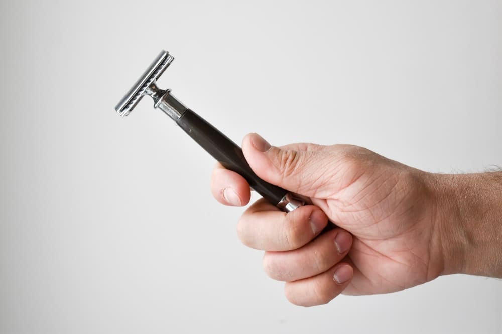 Close-up image of a hand holding a single blade razor against a plain gray background, illustrating the simplicity and traditional design of single blade razors in the context of the single blade razor vs multi blade razor debate.