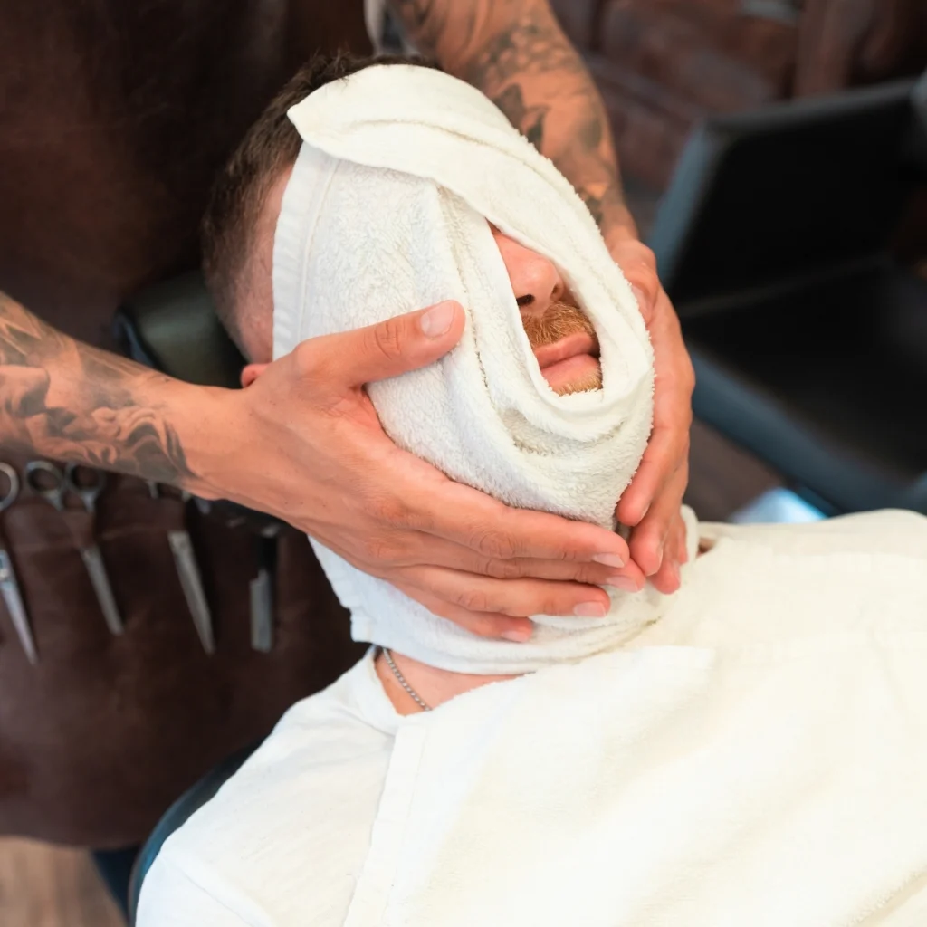 Barber applying a warm towel to a man's face before a hot towel shave.