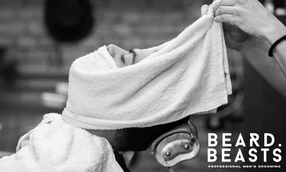 Barber applying a hot towel to a man’s face during a classic grooming shave, showing the benefits of a hot towel shave.