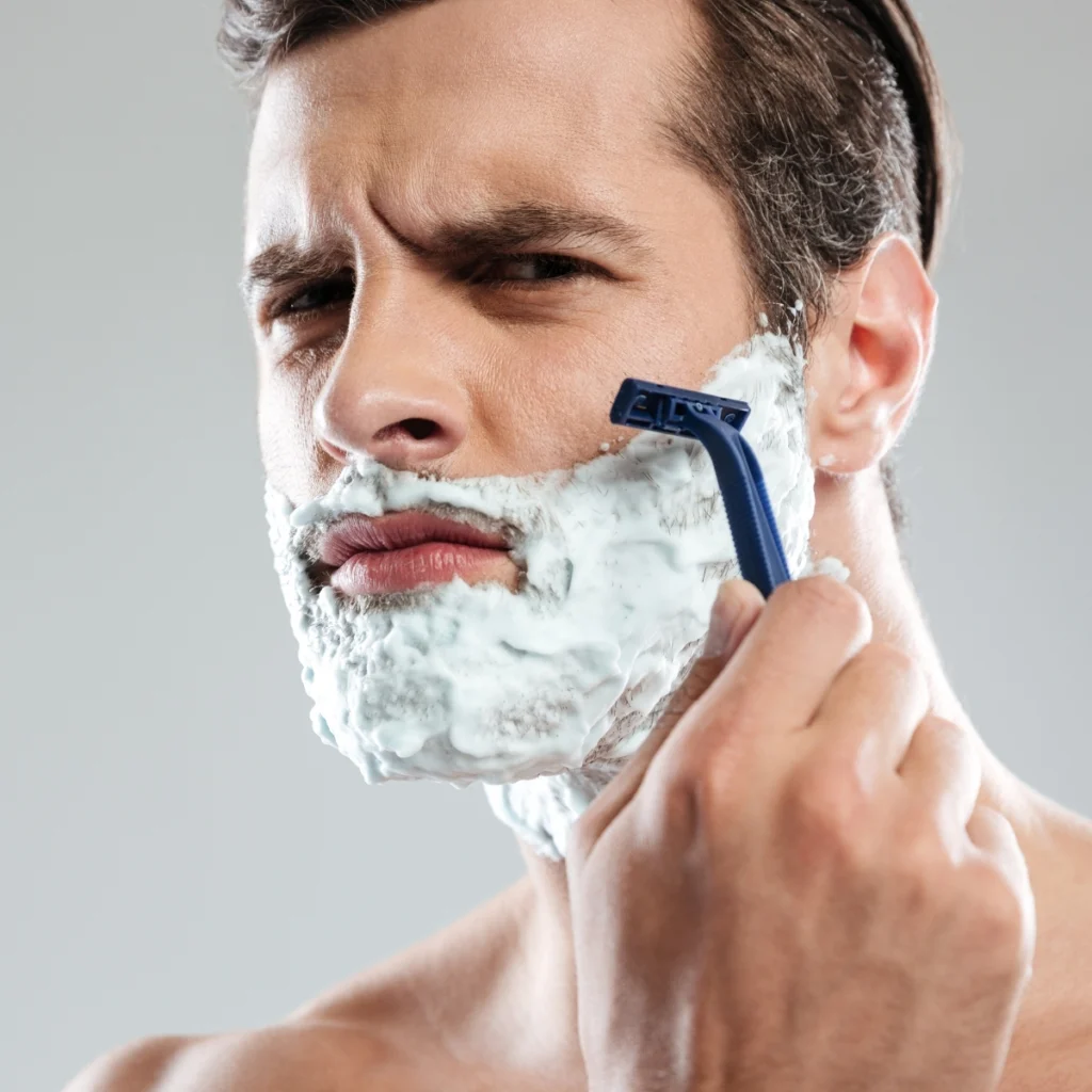 Man wet shaving with a cartridge razor and shaving cream on his face