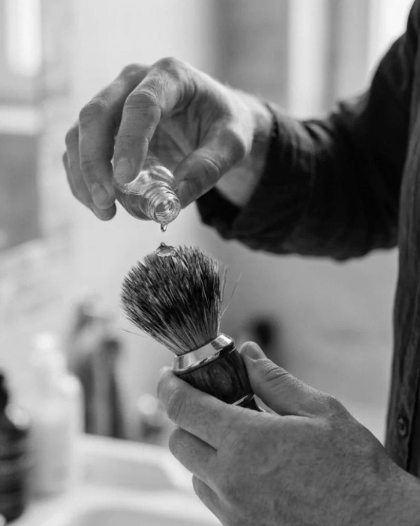 Man applying a small amount of cleaner to a shaving brush in a bathroom sink, showing that far less cleaner is needed to clean a shaving brush properly