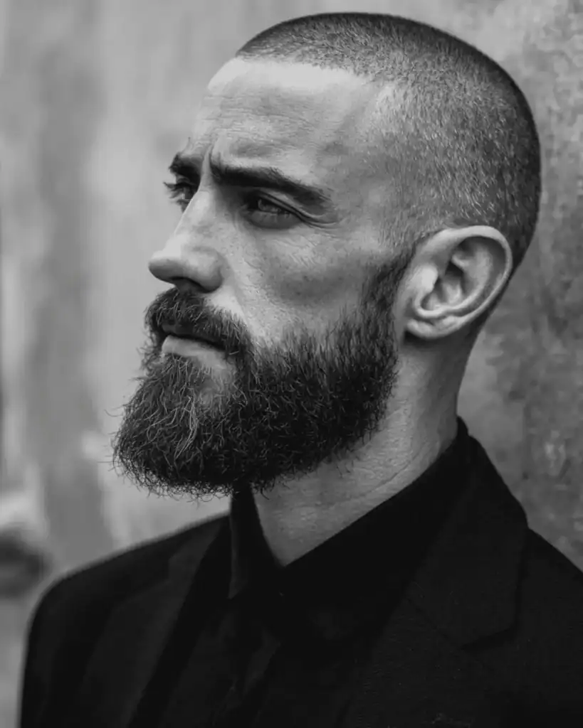 Side profile of a man with a short buzz cut paired with a thick, well-groomed full beard.