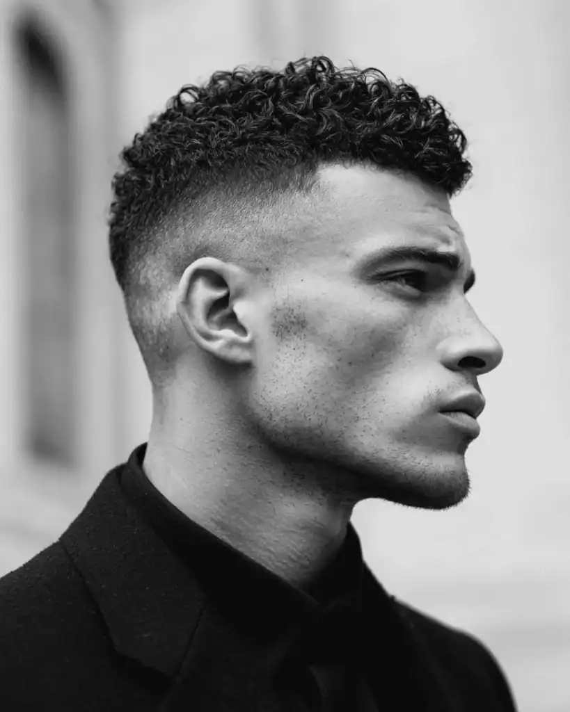 Side profile of a man with textured short curly hair and a sharp skin fade.