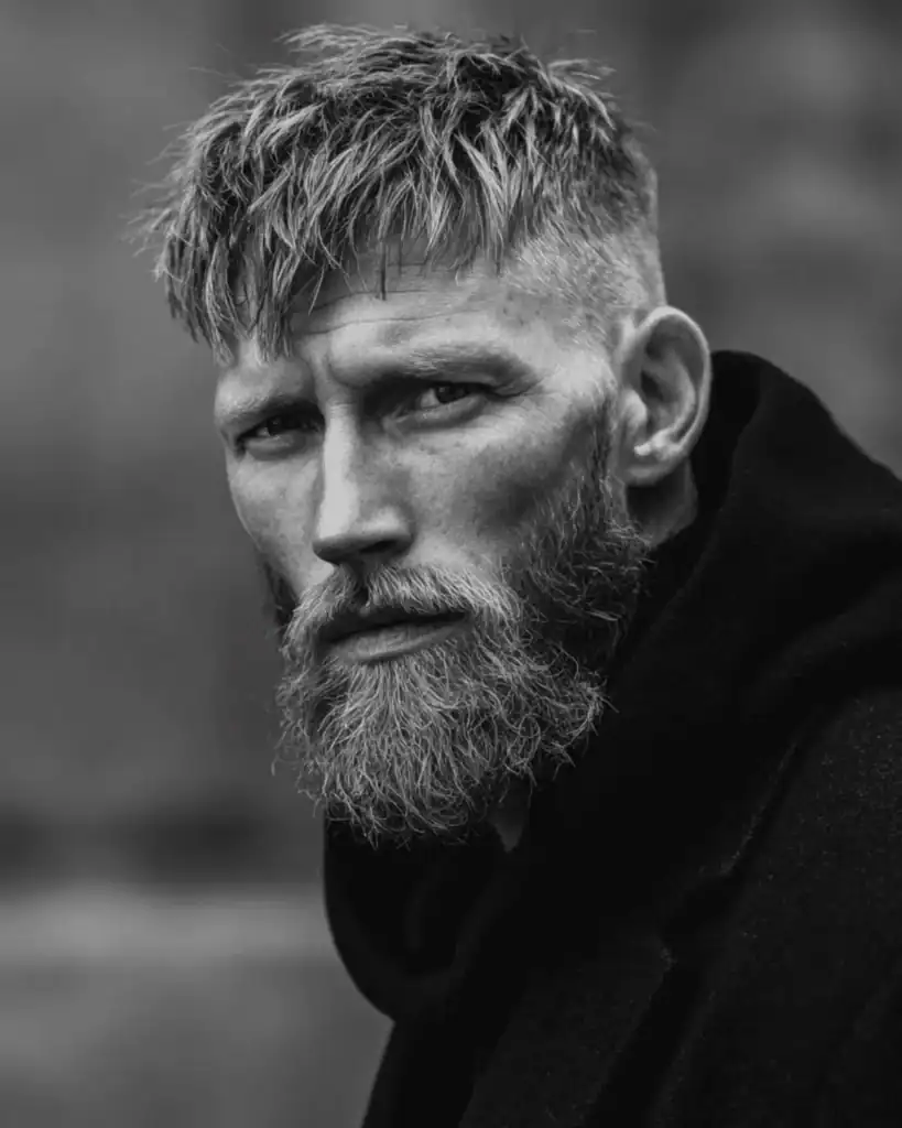 Black and white portrait of a man with a short textured crop haircut and a rugged, medium-length full beard.